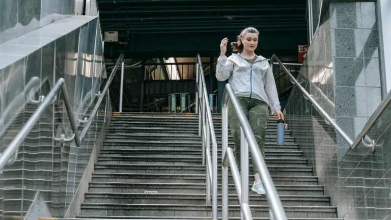 Woman in sportswear descending stairs, holding a water bottle, outdoors.