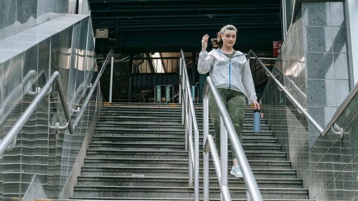 Woman in sportswear descending stairs, holding a water bottle, outdoors.