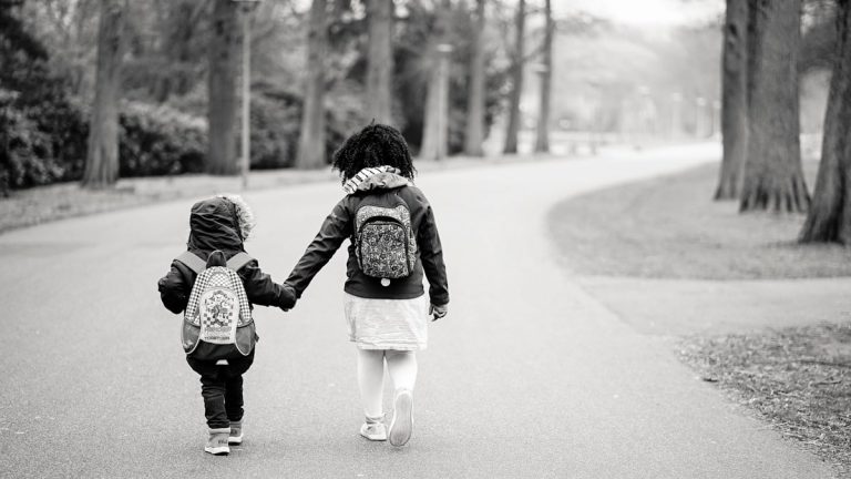 grayscale photography of two toddlers walking on road