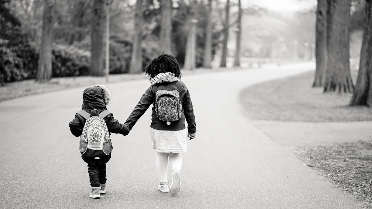 grayscale photography of two toddlers walking on road